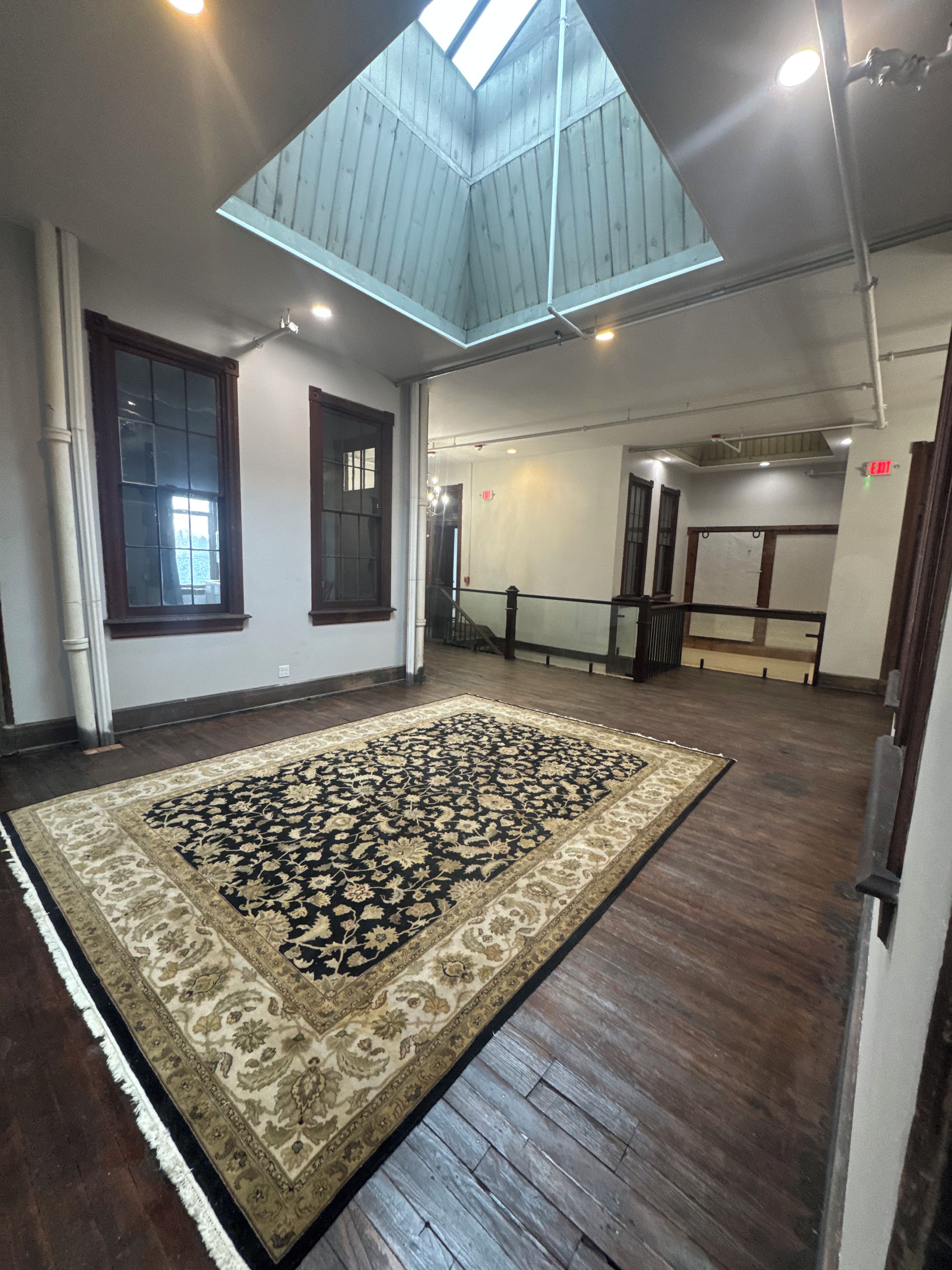 A spacious room with a large patterned rug, wooden flooring, and a skylight.