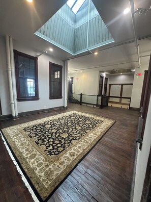 A spacious room with a large patterned rug, wooden flooring, and a skylight. - Experience a Victorian Renovation with Modern Conveniences Downtown In Urbana,OH (Urbana)