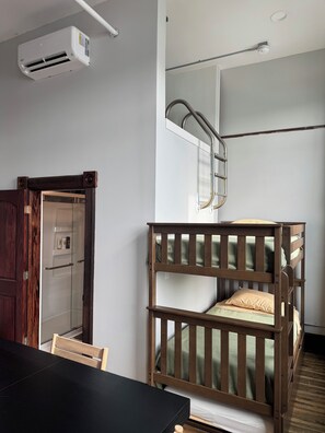 A room with a bunk bed, a wooden table, a chair, an air conditioning unit, and a glass-enclosed shower area. - Experience a Victorian Renovation with Modern Conveniences Downtown In Urbana,OH (Urbana)