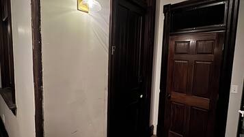 A hallway with a wooden door, a light fixture, and a doormat.