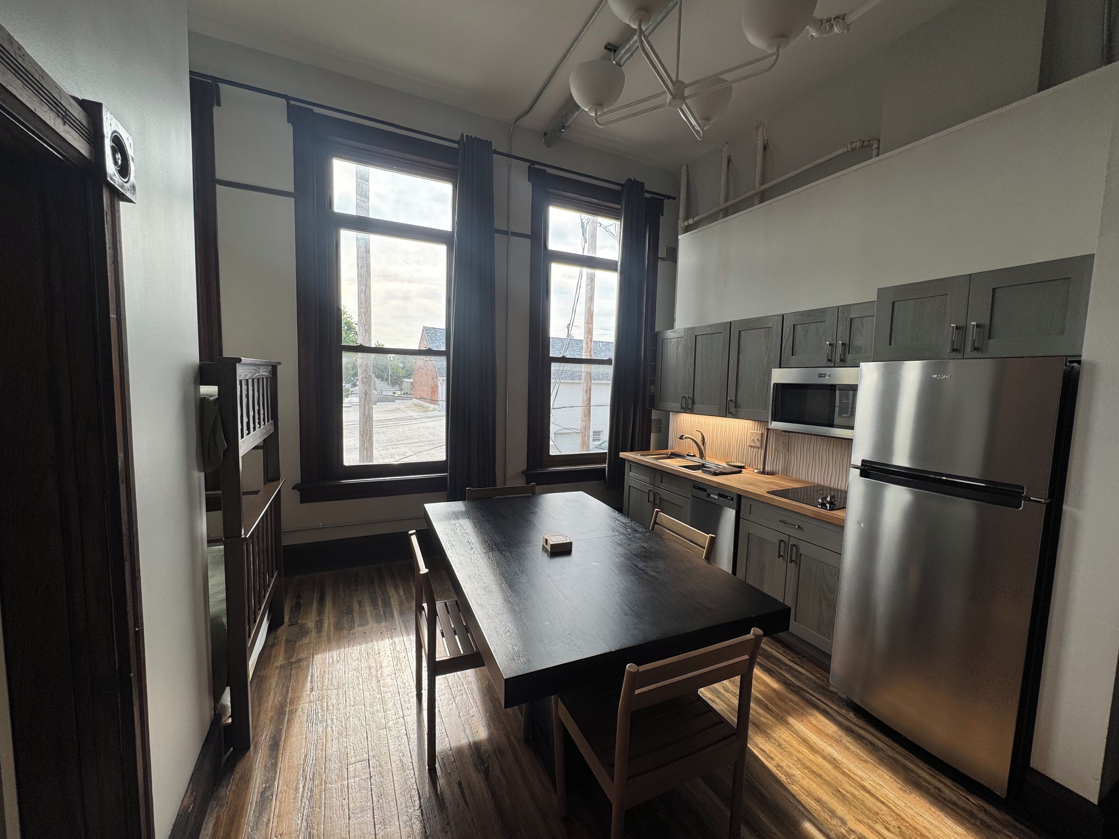A modern kitchen with a wooden table, a stainless steel refrigerator, and a window with curtains.