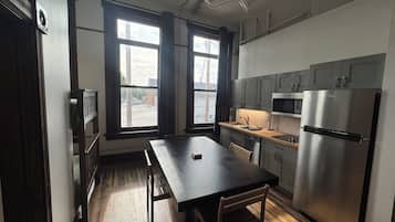 A modern kitchen with a wooden table, a stainless steel refrigerator, and a window with curtains.
