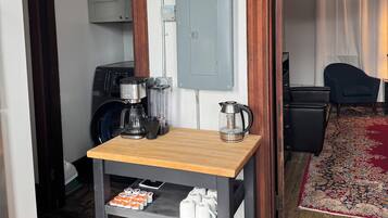 A compact room with a wooden table, a washing machine, a coffee maker, and a power outlet box.