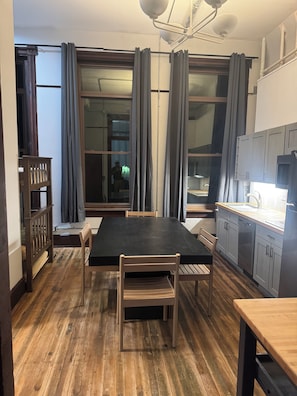 A dining area with a black table, wooden chairs, and a view through large windows with curtains.