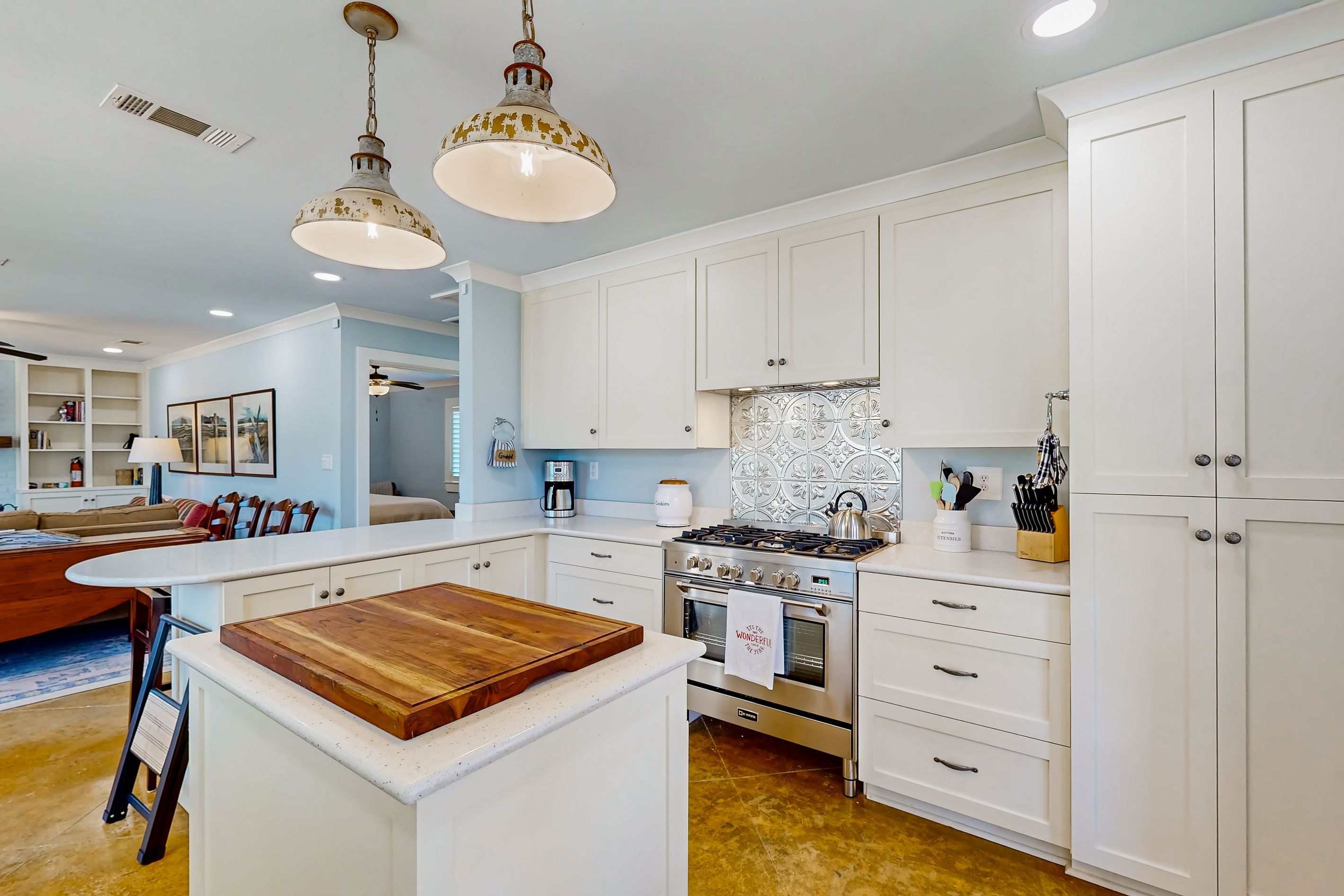 A modern kitchen with white cabinetry, a central island with a wooden countertop, stainless steel appliances, and pendant lighting.