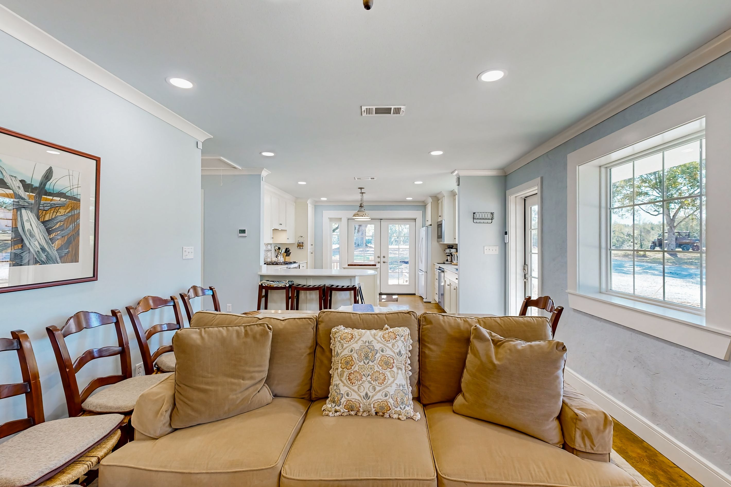 A living room with a beige sofa, wooden chairs, a dining area, and a kitchen in the background.