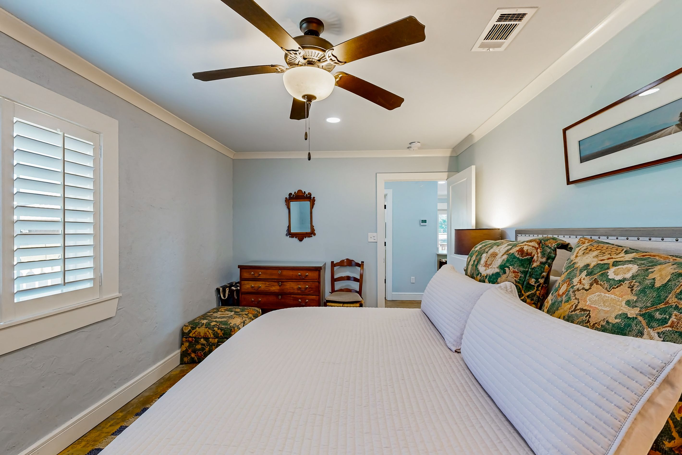 A bedroom with a bed, a ceiling fan, a dresser, a chair, and a window with blinds.