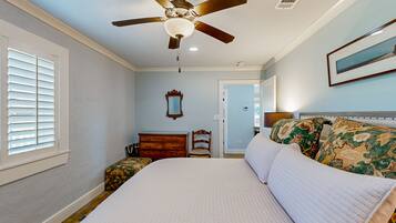 A bedroom with a bed, a ceiling fan, a dresser, a chair, and a window with blinds.