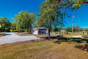 A small house with a porch, surrounded by trees and a gravel driveway.