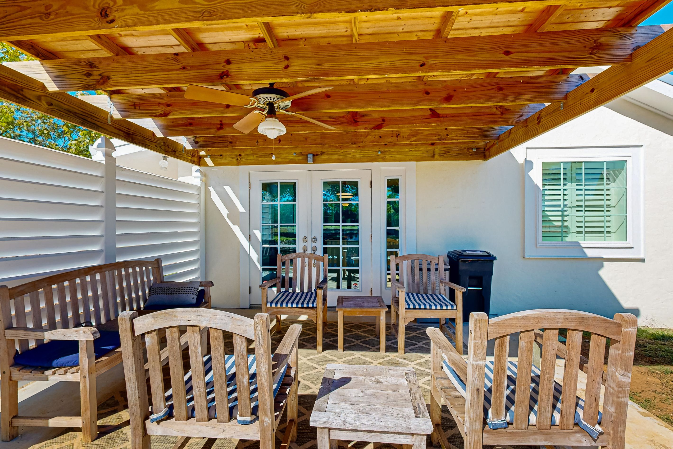An outdoor patio with wooden furniture, a ceiling fan, and a view of a white house with a window.
