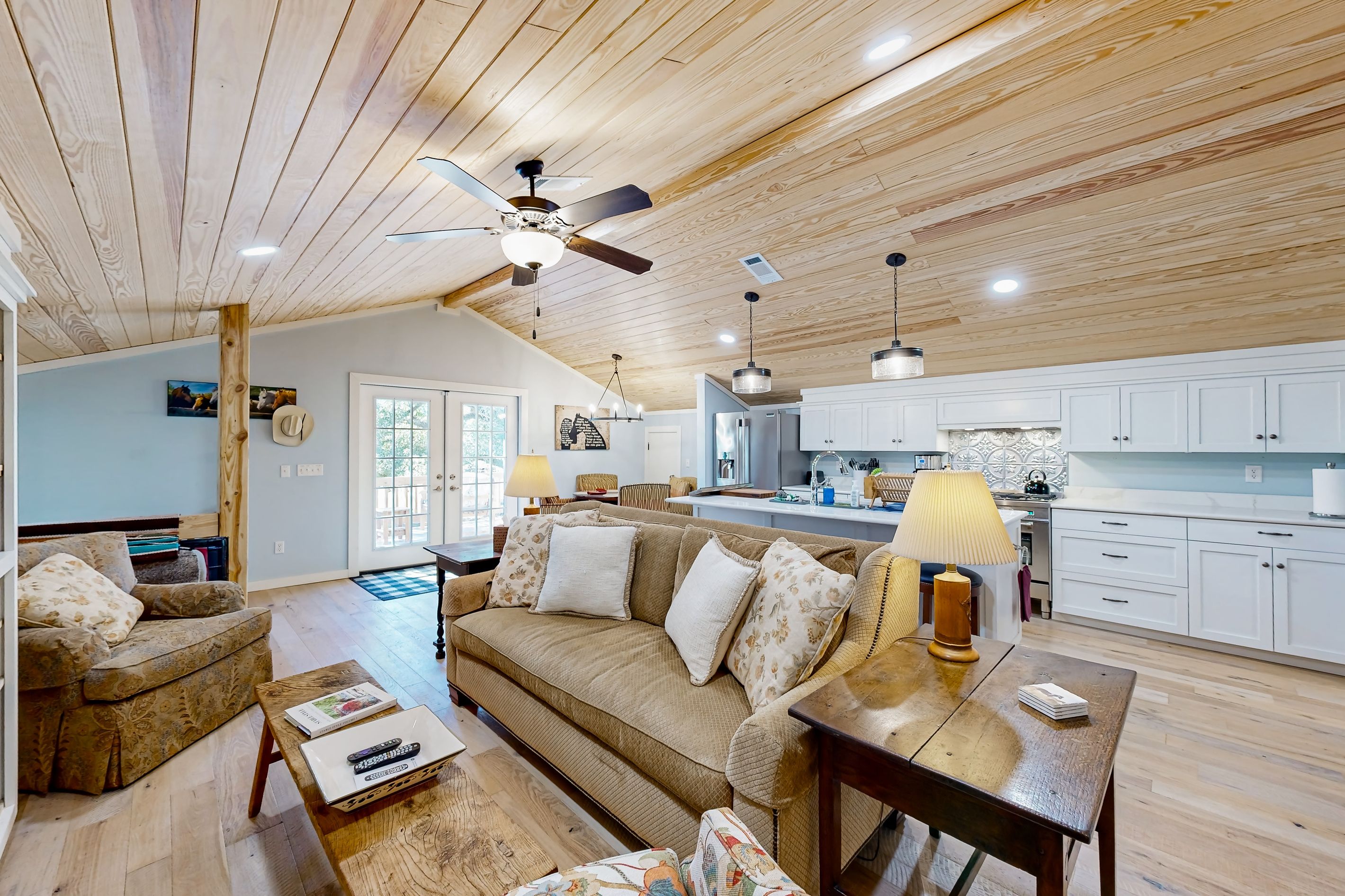 A spacious living area with a high ceiling, wooden beams, a sofa set, a dining table, and a kitchen in the background.
