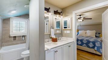 A bathroom with a bathtub, toilet, and sink, and a bedroom with a bed and ceiling fan.