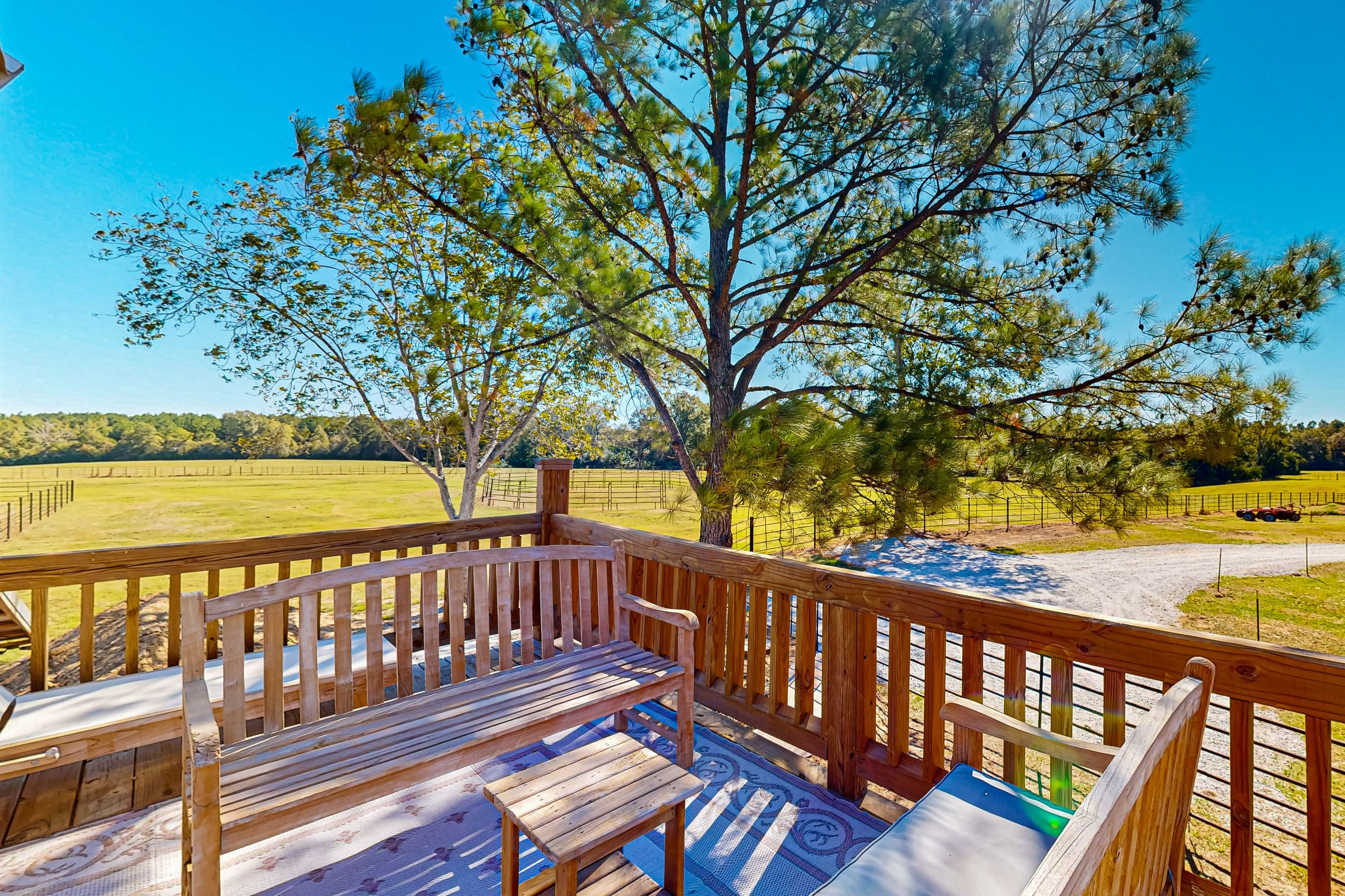 A wooden deck with benches and a view of a tree and fields.