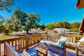 A wooden deck with a sofa and a table, overlooking a residential area with houses and trees.