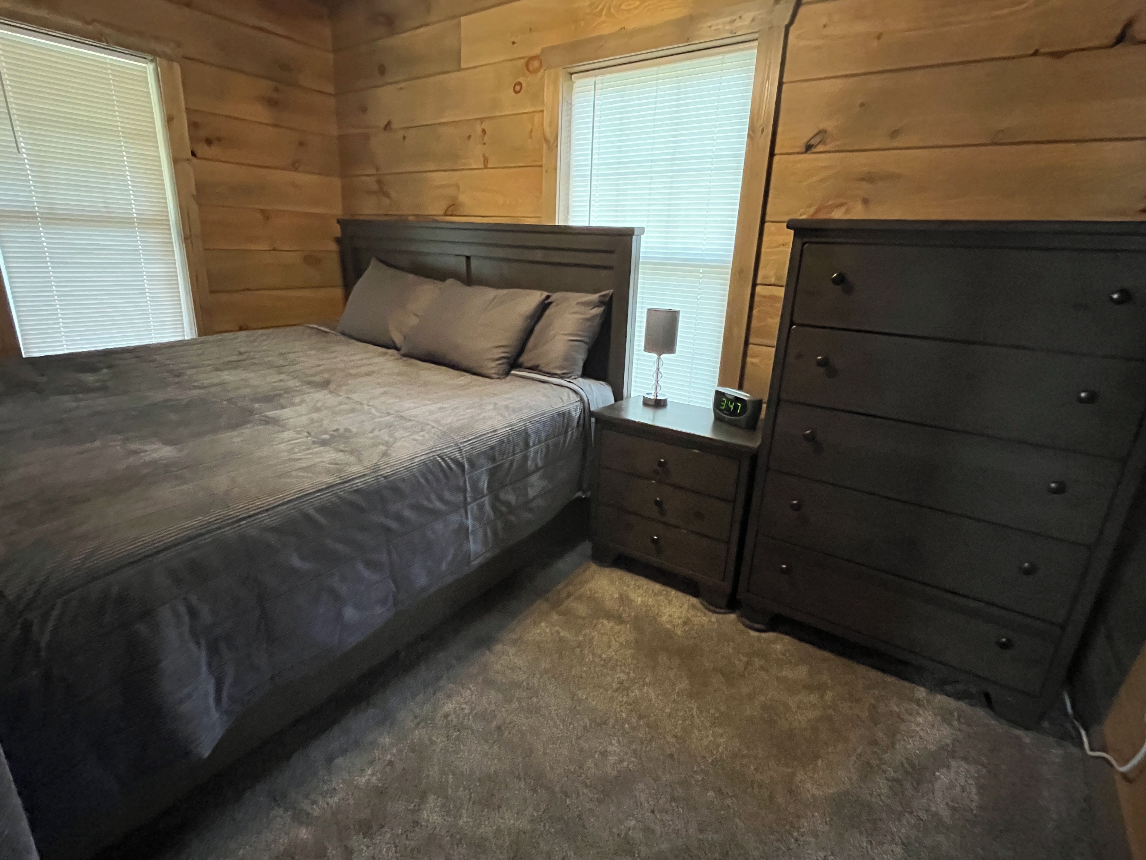 A bedroom with a bed, nightstand, dresser, and a window with blinds.