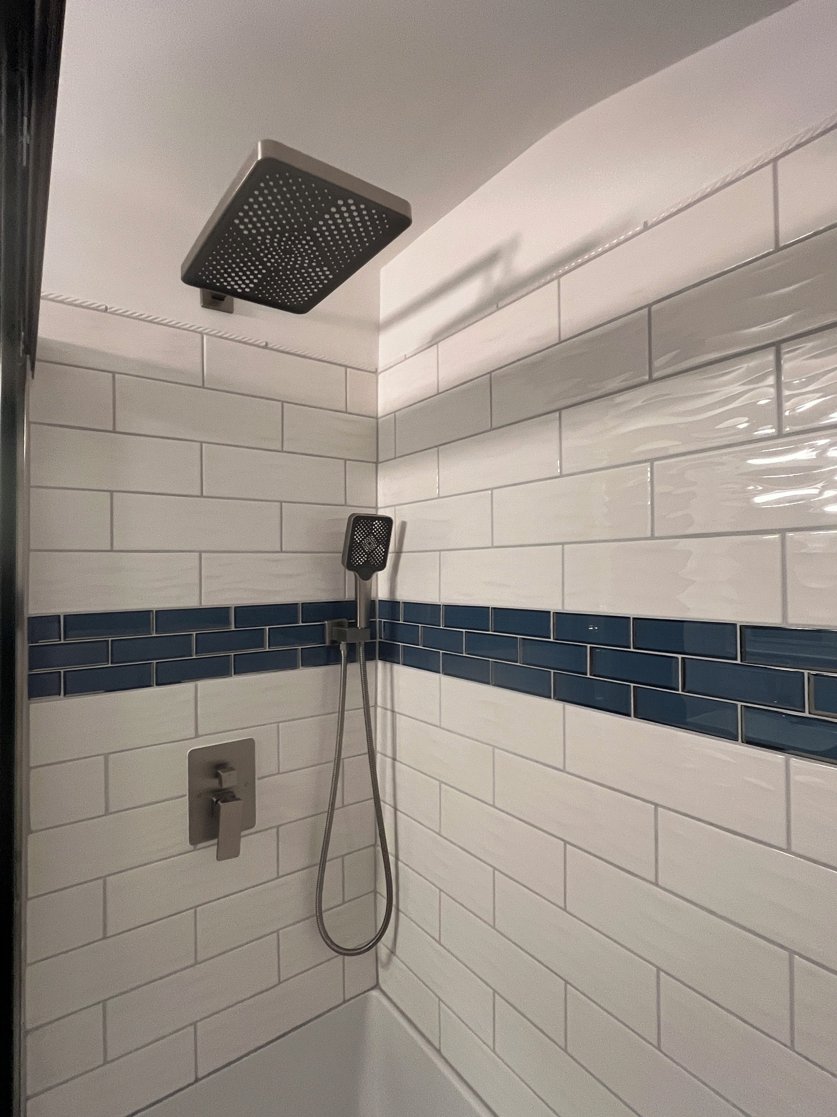 A shower area with white tiles and a blue accent border.