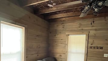 A room with a gray sectional sofa, wooden walls, and a ceiling fan.