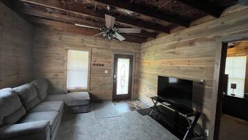 Ein rustikales Blockhaus-Interieur mit einer Couch, einem Kamin, einem Deckenventilator und Holzwänden.