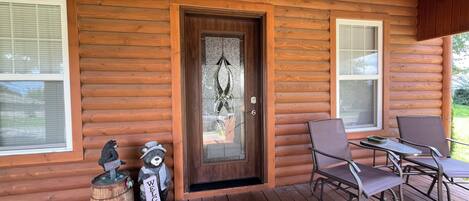 A wooden cabin with a porch, a door with a glass panel, and two chairs.
