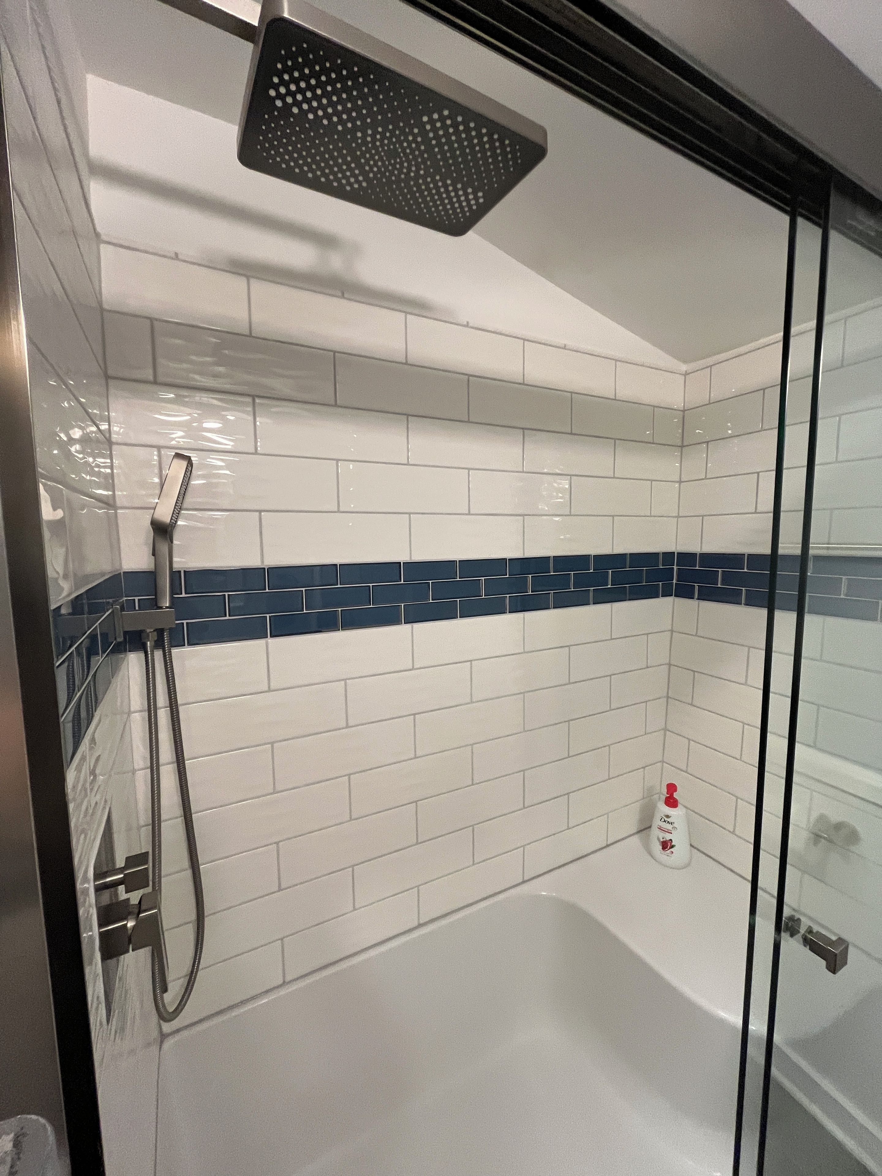 Une salle de bain moderne avec des carreaux de métro blancs, une bordure bleue décorative, une douche à l’italienne et un pommeau de douche à main.