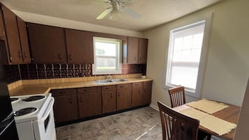 A kitchen with wooden cabinets, a stove, a sink, and a dining area with a table and chairs.