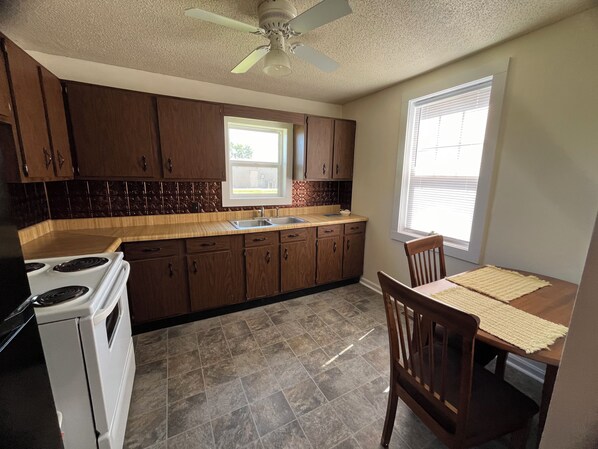A kitchen with wooden cabinets, a stove, a sink, and a dining area with a table and chairs.