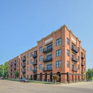 A multi-story brick building with balconies, a gated entrance, and a clear sky. - Grand Junction Football Condo! Walkable to Stadium and golf cart service. (Starkville)