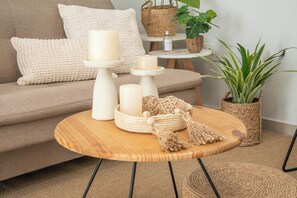 Een gezellige zithoek met een ronde houten tafel, kaarsen, een gebreide kussen en een geweven mand.