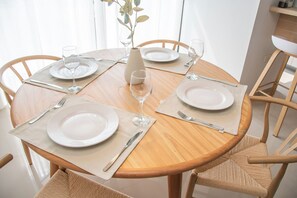 Une table de salle à manger ronde en bois, dressée avec de l’assiette blanche, des couverts et des verres, et entourée de chaises en osier.