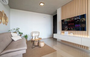 Ein modernes Wohnzimmer mit einer Couch, einem runden Tisch mit einem Stuhl, Topfpflanzen und einem an der Wand befestigten Netflix-Display.