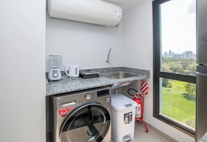 Une cuisine compacte équipée d’un lave-linge, d’une machine à café et d’un mixeur, le tout posé sur le plan de travail.