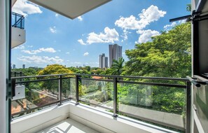 A balcony with a glass railing overlooking a cityscape with buildings and greenery. - Asunción 2BR | Pool, Gym, Balcony & Parking (Asunción)