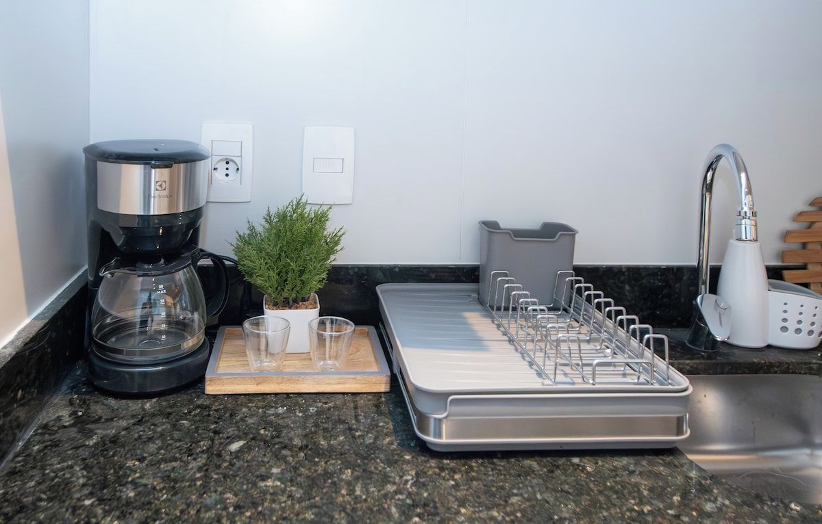 A kitchen with a coffee maker, a plant, a tray with utensils, and a sink.