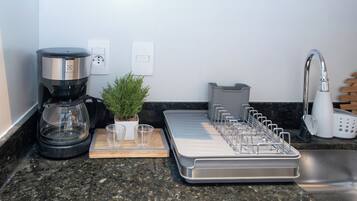 A kitchen with a coffee maker, a plant, a tray with utensils, and a sink.