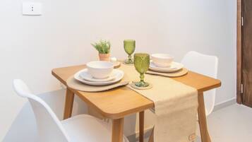 A dining area with a table set for two, white chairs, a small potted plant, and a framed artwork above.