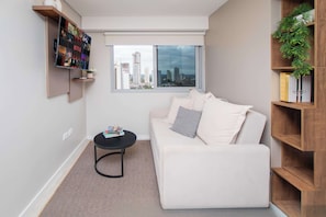 A modern living room with a white sofa, a small black coffee table, a bookshelf, and a TV mounted on the wall displaying a Netflix interface. - Modern Studio with Pool&Gym near Paseo La Galeria (Asunción)