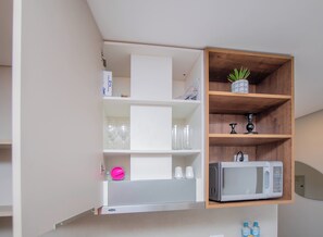 Une cuisine équipée d’un four à micro-ondes encastré, d’une étagère avec une plante en pot et d’un meuble contenant des verres à vin.