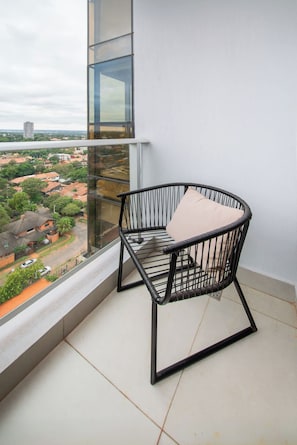 A balcony with a black metal chair and a cushion, overlooking a residential area with houses and a distant building. - Modern Studio with Pool&Gym near Paseo La Galeria (Asunción)