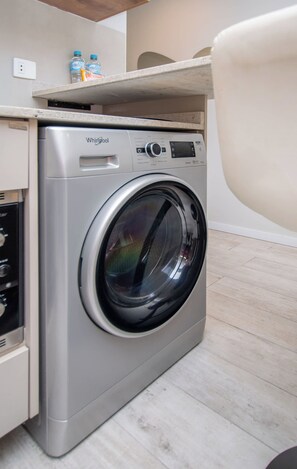 A Whirlpool washer in a compact space with a countertop above it, a water bottle, and a bag of snacks. - Modern Studio with Pool&Gym near Paseo La Galeria (Asunción)