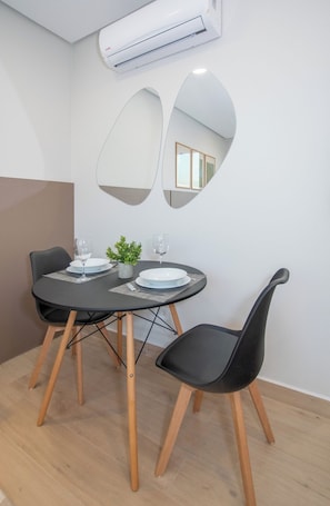 A modern dining area with a round table, two black chairs, a small potted plant, and a white air conditioning unit mounted on the wall. - Modern Studio with Rooftop Pool, City Views & WiFi (Asunción)