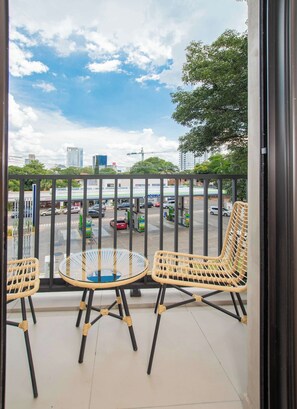 Ein Balkon mit Korbstühlen und einem Glastisch, mit Blick auf eine belebte Straße mit Autos und einer Tankstelle.
