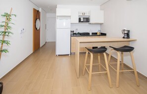 A modern kitchen with white cabinets, a microwave, a refrigerator, and two black bar stools. - Lumiere del Sol Studio | Pool, Balcony & City View (Asunción)