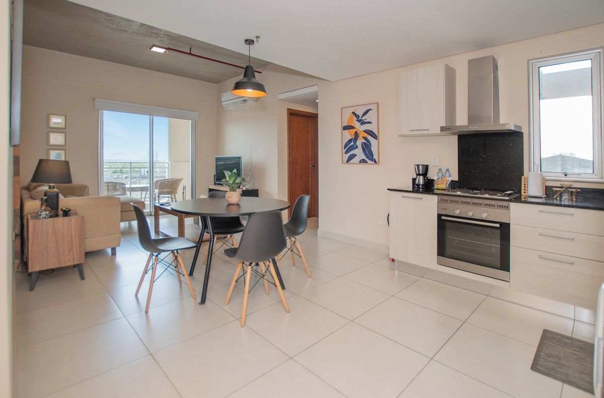 A modern kitchen with a dining area, a large window, and a balcony.