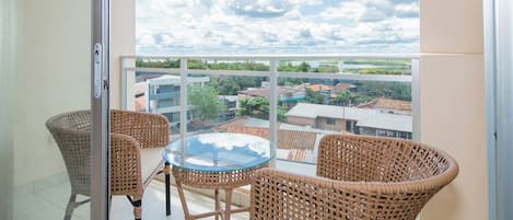 A balcony with wicker furniture and a glass table, overlooking a residential area with houses and a clear sky.