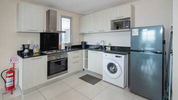 A modern kitchen with a stainless steel refrigerator, a built-in oven, a microwave, and a washing machine.