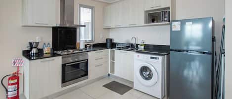 A modern kitchen with a stainless steel refrigerator, a built-in oven, a microwave, and a washing machine.