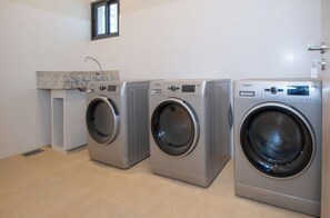 Drei frontbeladene Waschmaschinen hintereinander, eine Arbeitsplatte mit Spüle und ein Fenster darüber.