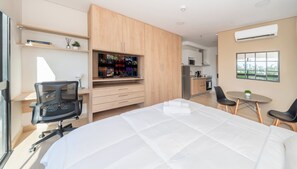 Ein modernes Schlafzimmer mit einem großen Bett, einem Schreibtisch mit Computer, einem Fernseher und einer Küchenzeile.