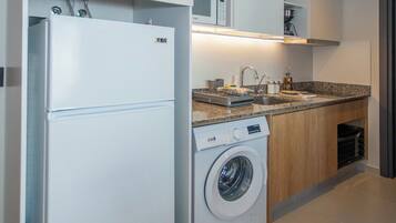 Una cocina compacta equipada con refrigerador, lavadora, microondas y un lavabo con encimera.
