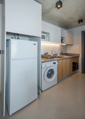 Una cuina compacta amb nevera, rentadora, microones i un rentat amb taulell.